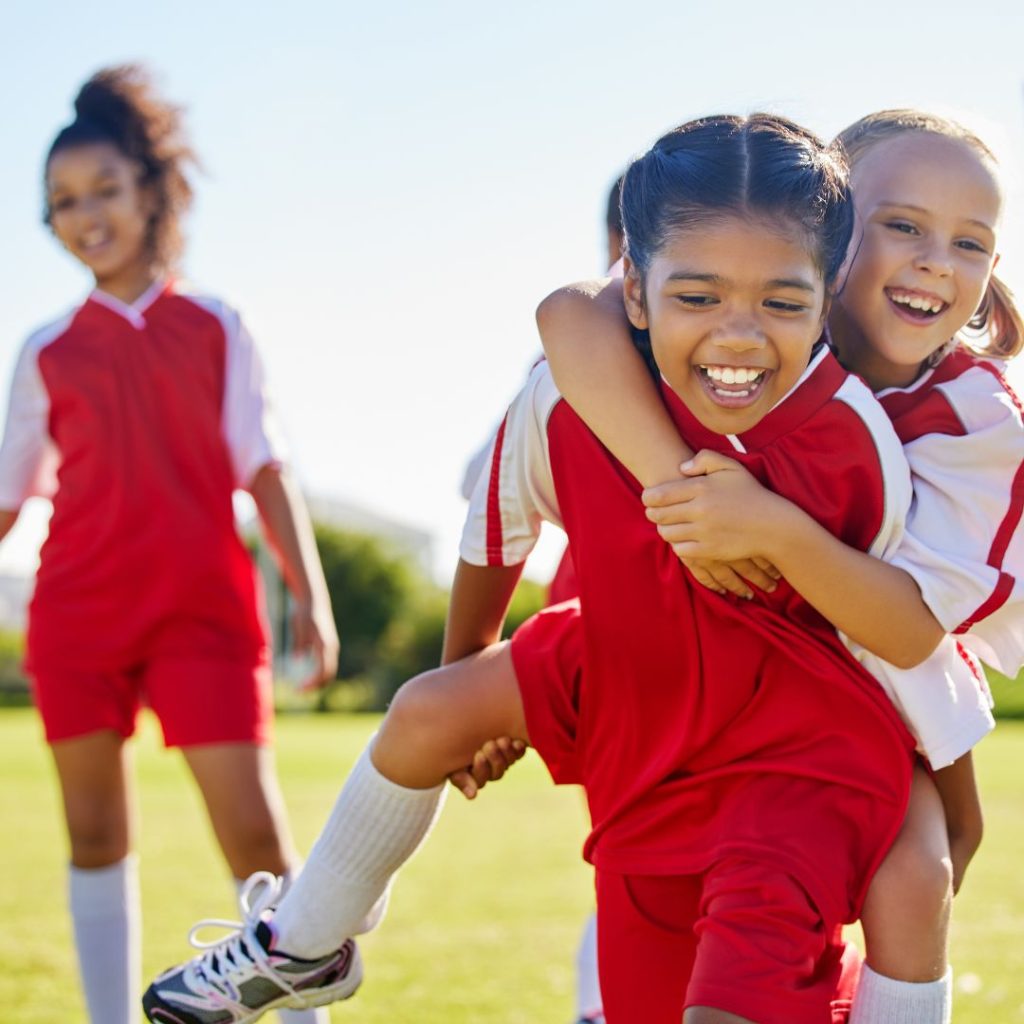A happy group of three young girls dressed in football kits are all smiles in the sunshine to represent this blog about the best children's sports franchise businesses for sale in the UK