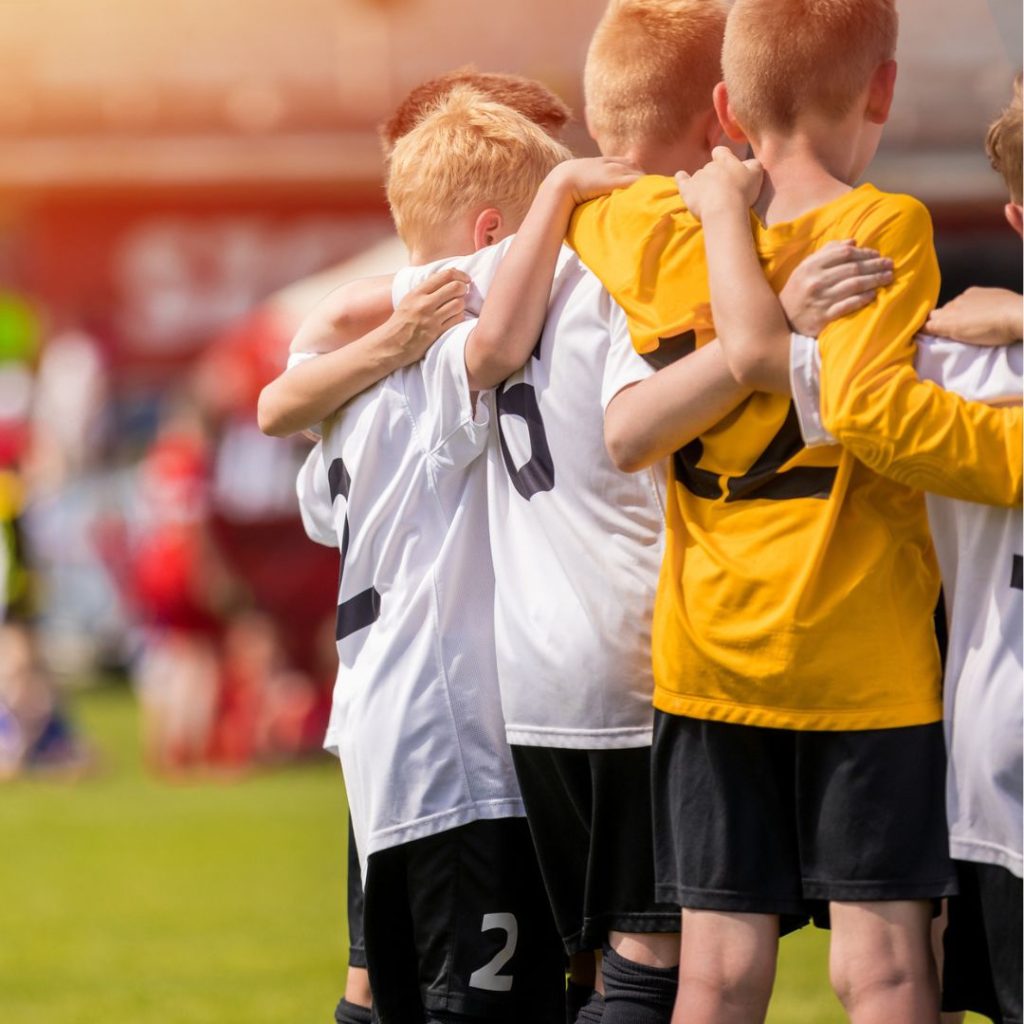 A group of young lads in football kits stand arm in arm in a circle at the side of a football pitch to represent this blog about the best children's sports franchise businesses for sale in the UK