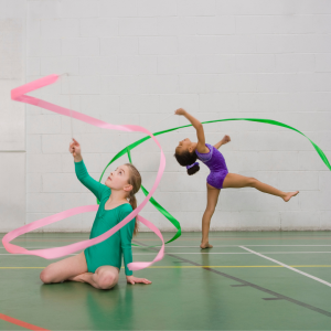 Two young dancers in leotards move in a dance space whilst twirling long ribbons to represent this blog about the best children's dance franchise businesses for sale in the UK