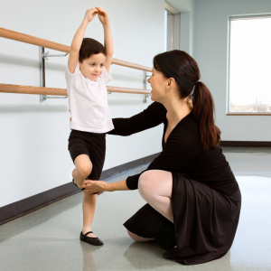 A dance teacher helps a young boy with his ballet dance positions in a studio setting and both wear dance clothes to represent this blog about the best children's dance franchise businesses for sale in the UK