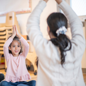 A yoga teacher demonstrates a yoga pose for a young girl to copy to represent this blog about the treasure trove of children's franchise opportunities for sale in the UK 