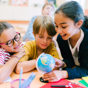 A small group of children smile as they gather around to study a globe of the world to represent this blog about teaching MFL to children with a Spanish language franchise 