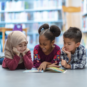 Three young children sit together in the floor of a library enjoying looking through a book together to represent this blog about franchise career opportunities for teachers thinking about leaving teaching
