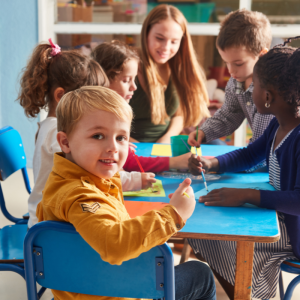 A group of children sit working at a table with one young boy turning to give a thumbs up to the camera to represent this blog about franchise career opportunities for teachers thinking about leaving teaching