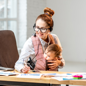 A busy young mum works at her desk on a phone call whilst also caring for her young baby to represent this blog about flexible career opportunities after maternity leave