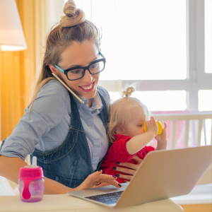 A young mum works at a laptop with her baby on her lap as she juggles work and family life to represent this blog about flexible career opportunities after maternity leave