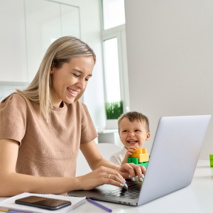 A young mum sits working at a laptop with her young son playing happily beside her to represent this blog about why buying a franchise is a brilliant option rather than starting a business from scratch 