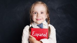 A young girl smiles to camera as she clutches a Spanish learning book to represent a blog on teaching MFL to children and running a Spanish language franchise
