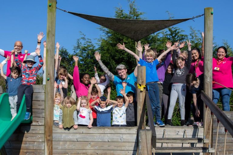 The leaders and children from childcare franchise Fun Fest joyfully pose with hands in the air in an outdoor adventure centre