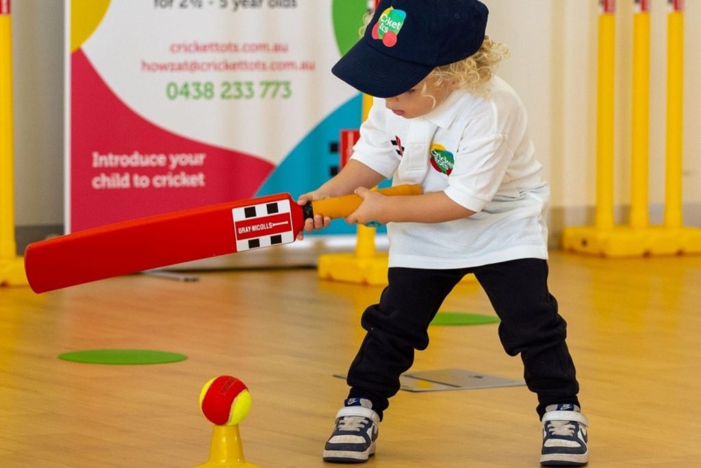 A toddler holds a cricket bat and hits the ball at an indoor session with Cricket tots, the unique children's sport franchise