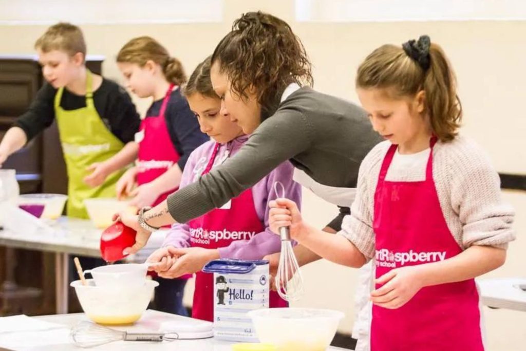 A cookery class with a teacher helping to measure ingredients and teaching cookery to children at a session with Smart Raspberry