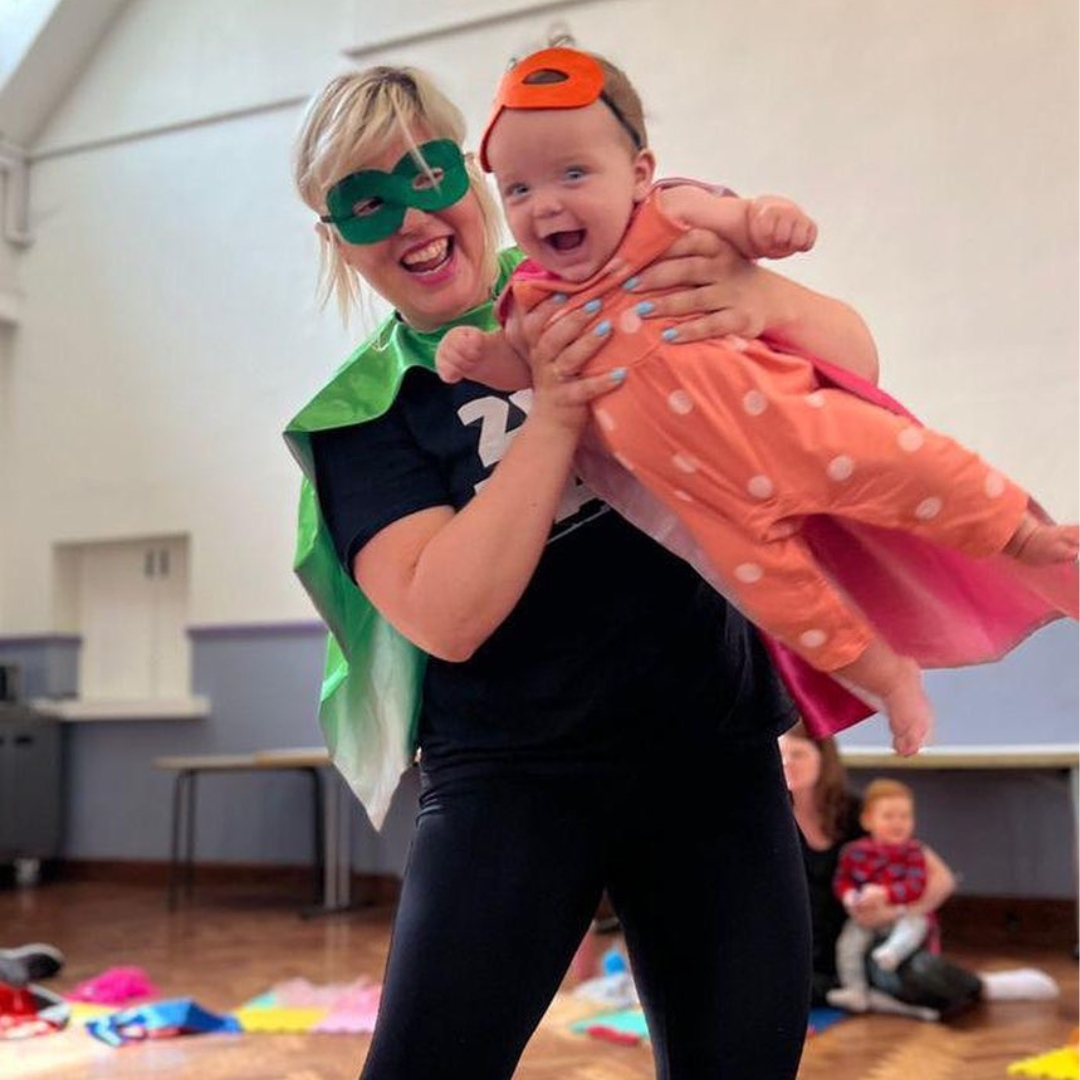Fun in full swing at children's franchise Zip Zap with a class leader dressed as a superhero helping a gleeful baby to pretend to fly through the air