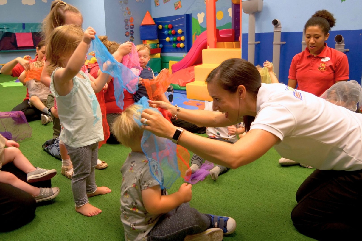 A fun session at Spanish franchise Mini Lingos is in full swing with young children gathered in a group on the floor enjoying a game with colorful scarves organised by two leaders