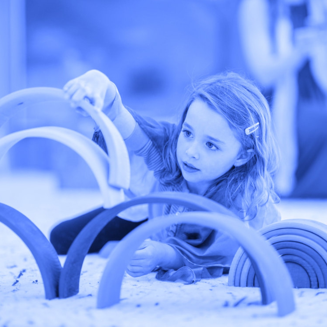 A young girl plays with a rainbow arch developmental sensory toy to represent the National College for Care and Education partnership opportunity