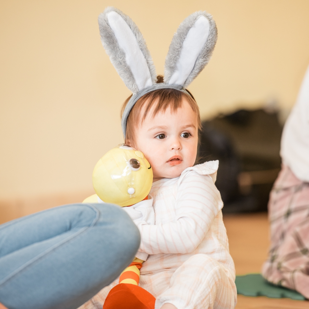 A toddler wears bunny ears and cuddles a Reg robot soft toy at a fun session with the Phonics with Robot Reg children's educational franchise