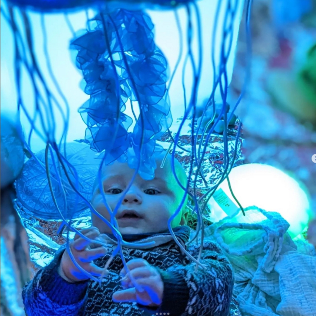 A baby reaches to touch and looks with interest at the blue sensory experience of lights and props at a session with children's sensory franchise Playtimes