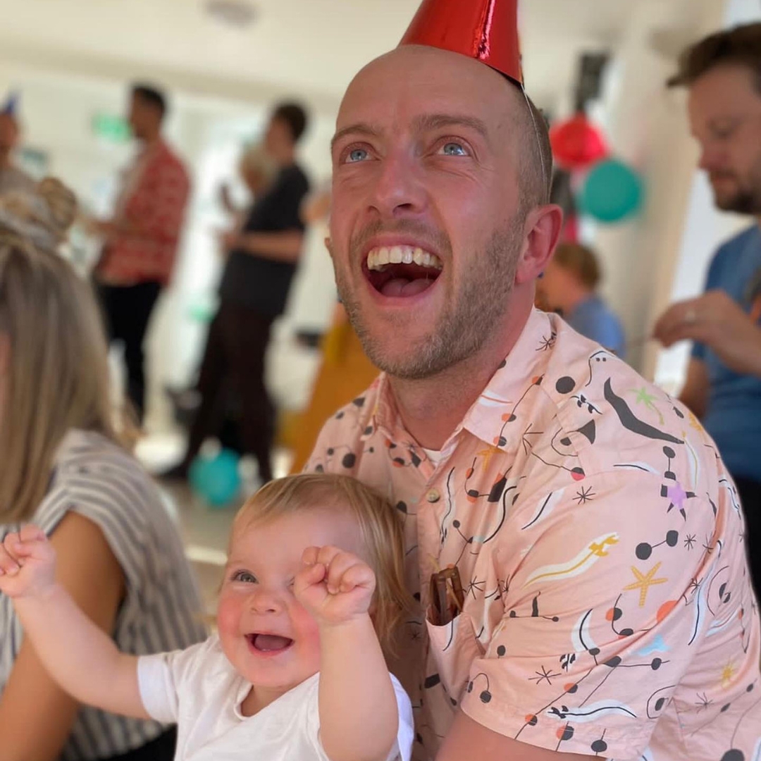 A dad and his toddler daughter are full of big smiles at a fun interactive event by Rock Out Baby the children's music franchise