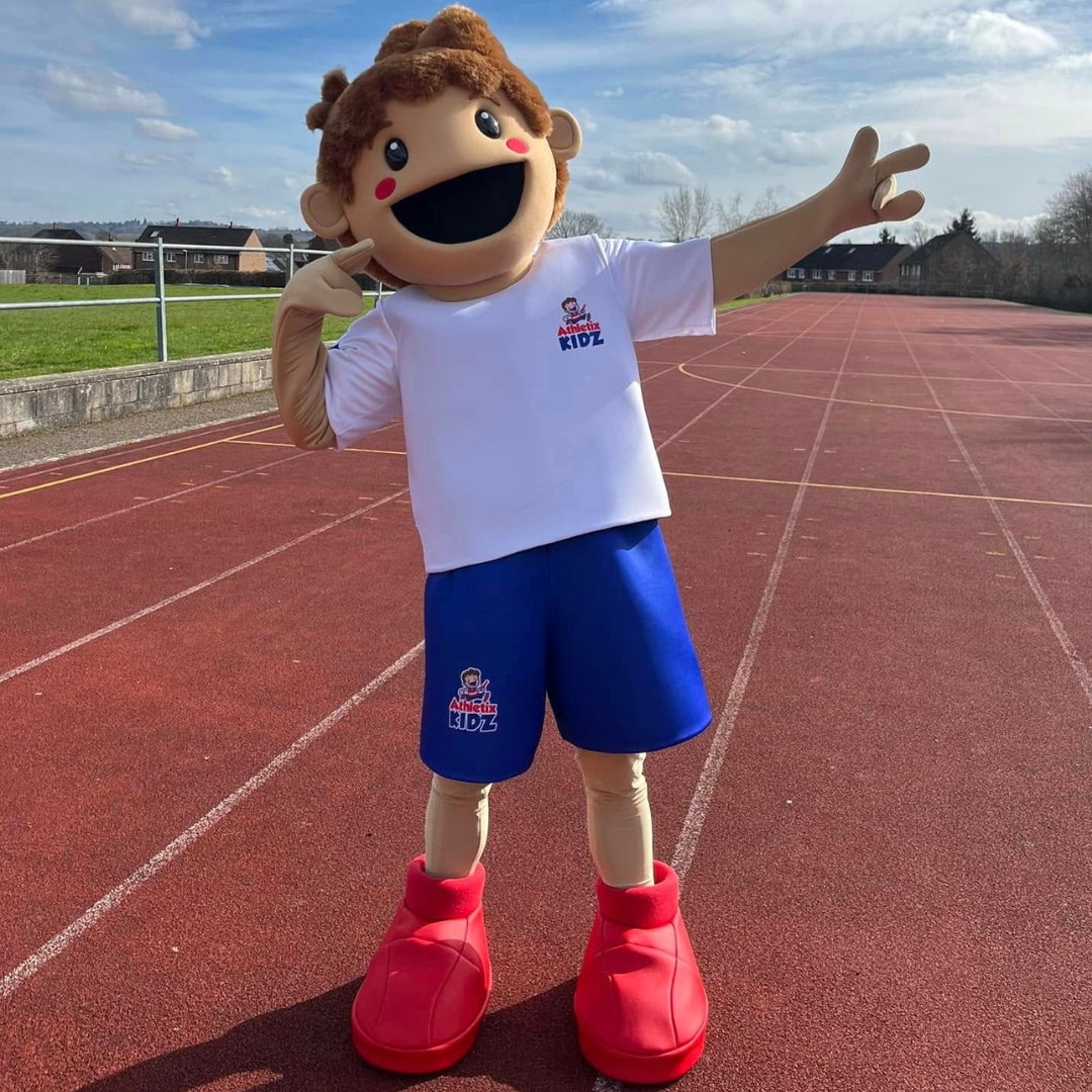 A large mascot character poses at the end of an outdoor running track representing the dynamic children's sports franchise Athletix Kidz