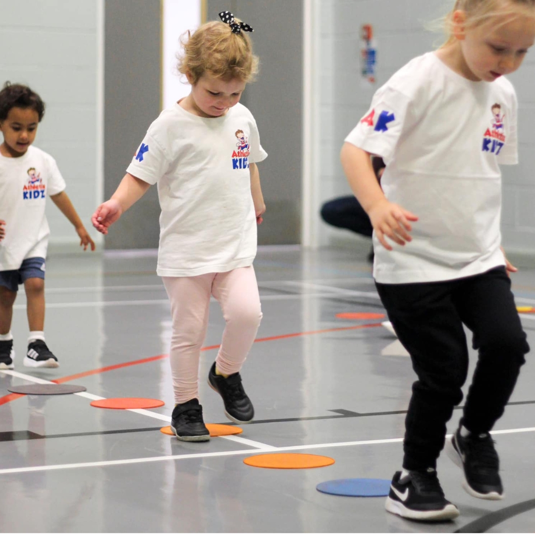 Young children take part in a stepping and balancing activity in an inside sports hall as part of the dynamic Athletix Kidz children's sports franchise