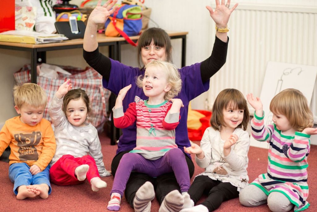 A group of young children smile and join in with a fun musical session from The Jolly Melodies Music Company