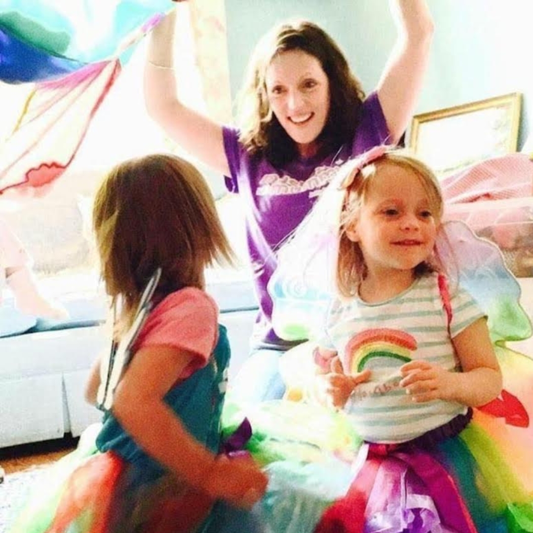 Two young girls in rainbow fairy costumes smile and play at an interactive session with The Jolly Melodies Music Company