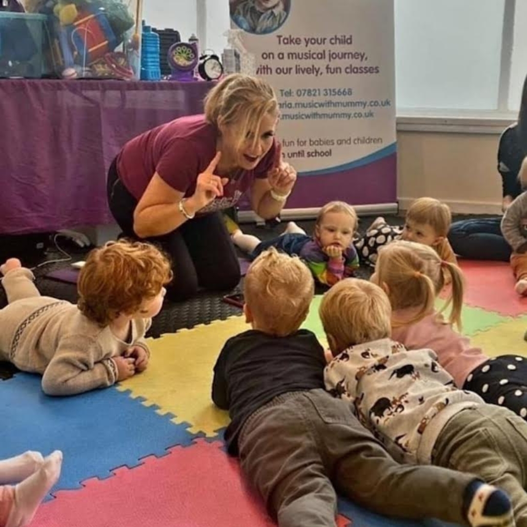 A group of small children gather in a circle around the leader at a fun musical session with music franchise brand The Jolly Melodies Music Company