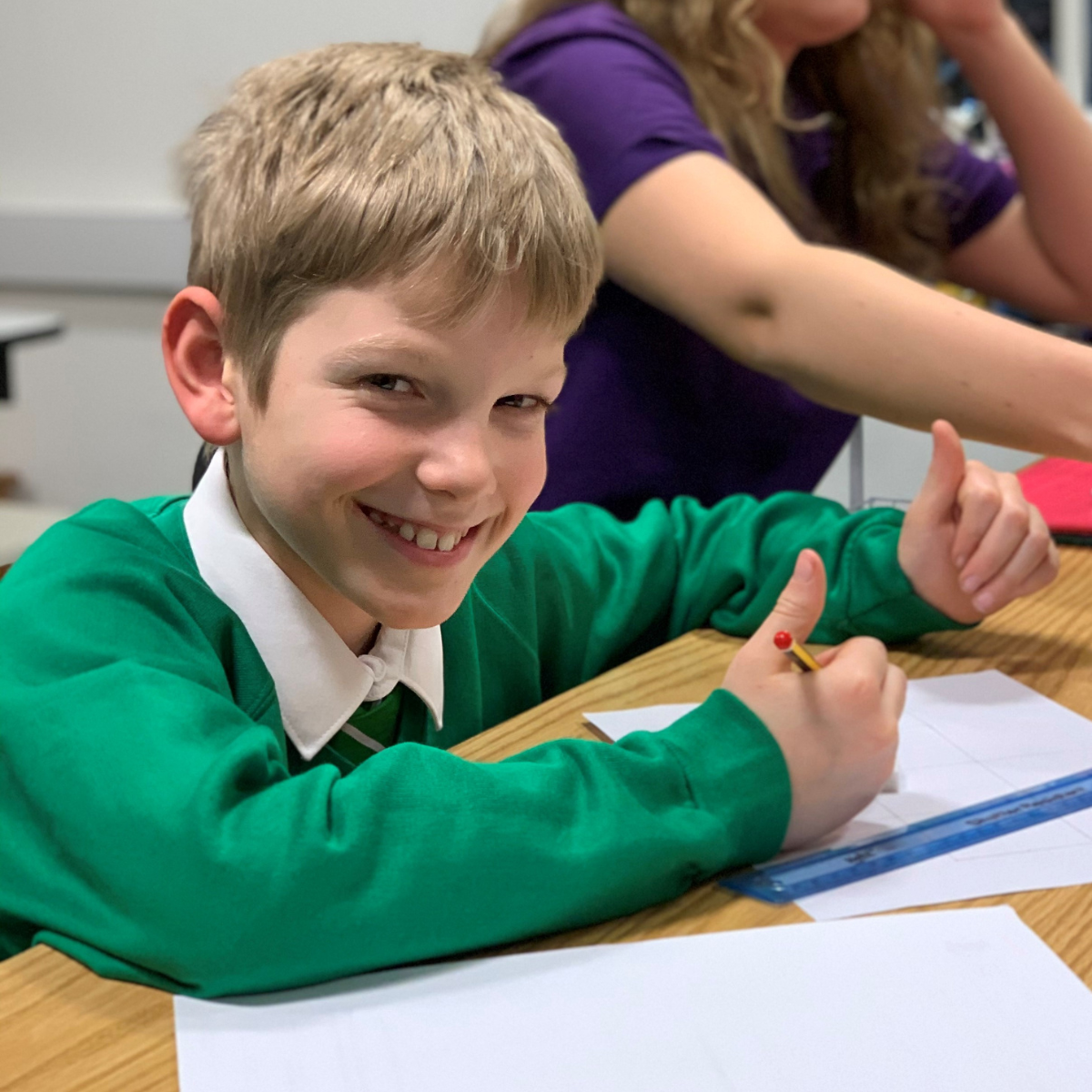 A young boy smiles at the camera with two thumbs up as he looks up from his worksheet at a tutoring session with MagiKats the education franchise business